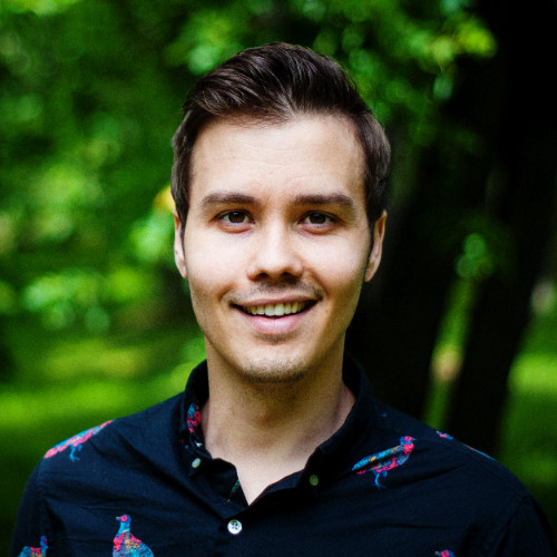 Ryan Barnett smiling in a colored peacock patterned shirt standing in front a forest background